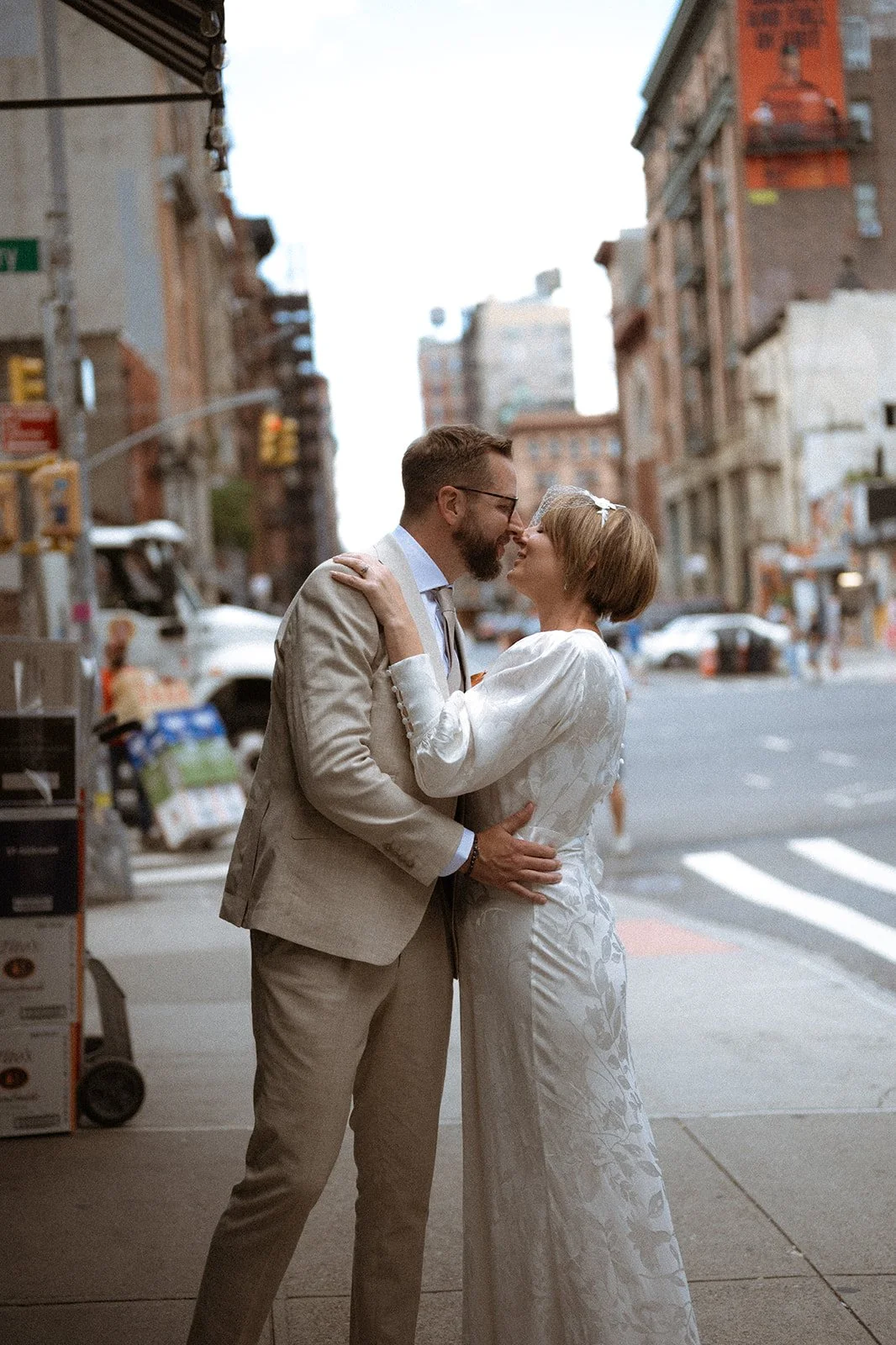 Bride and groom kissing on SoHo sidewalk with buildings and street lights behind them.