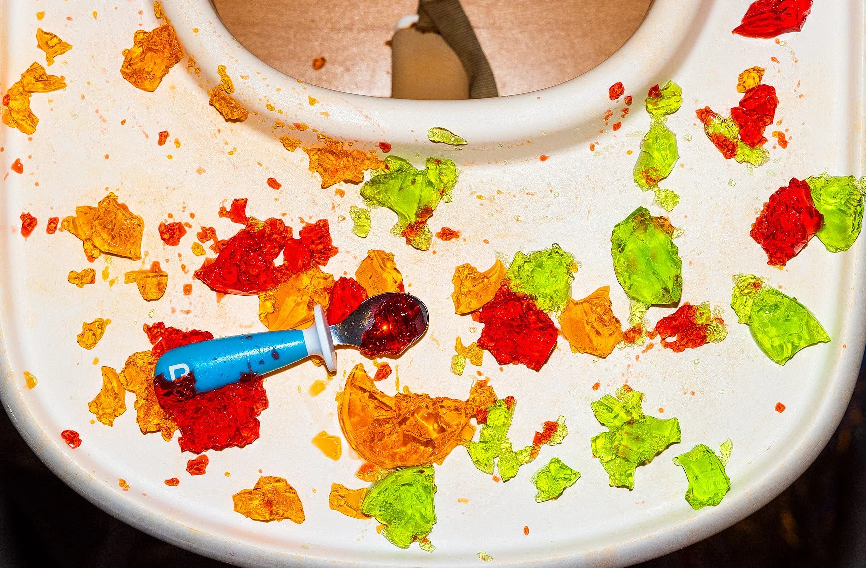 Colorful crushed jelly candies and a chewed jelly spoon on a white surface.