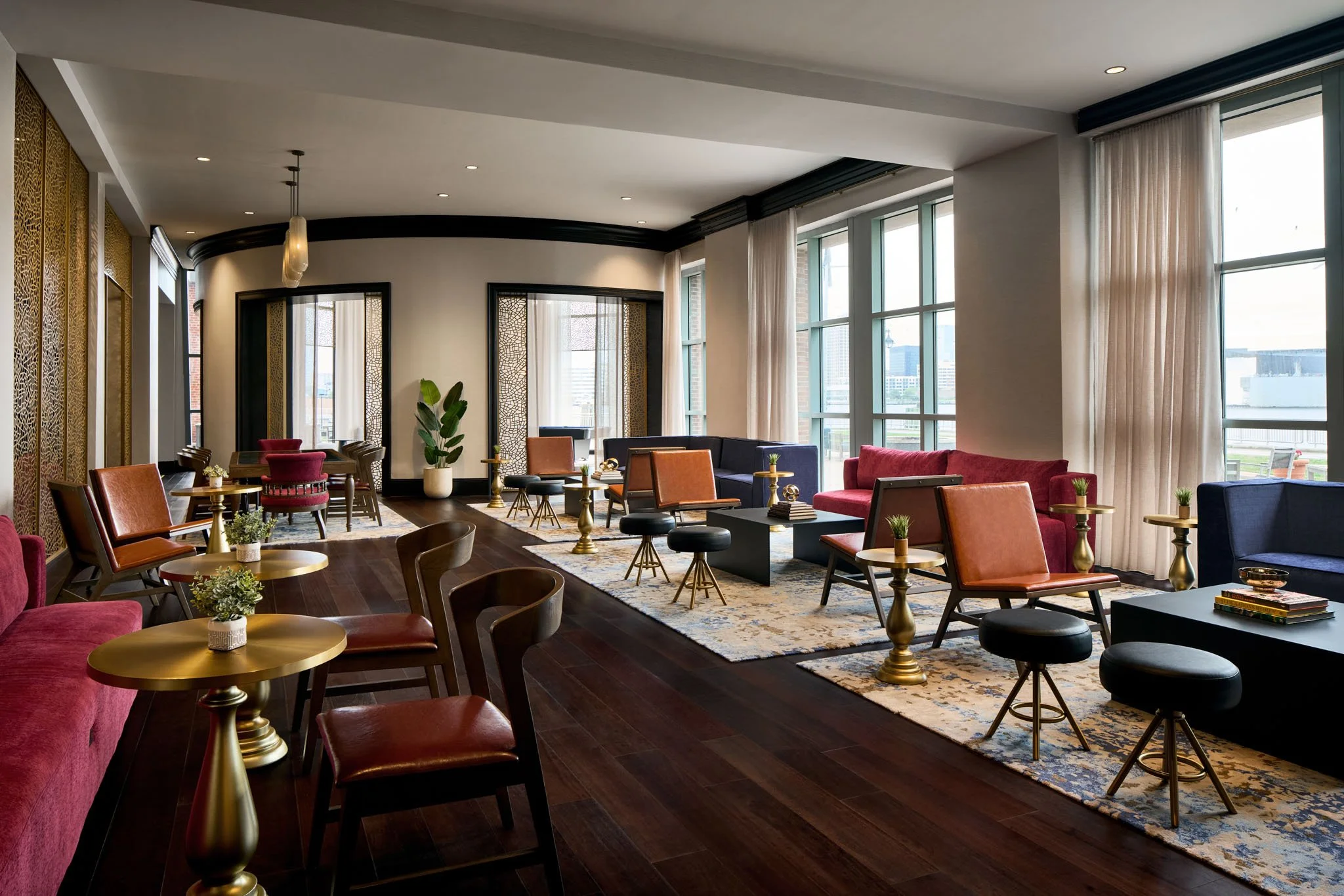 Modern lounge with large windows, colorful seating, gold accent tables, and a potted plant.