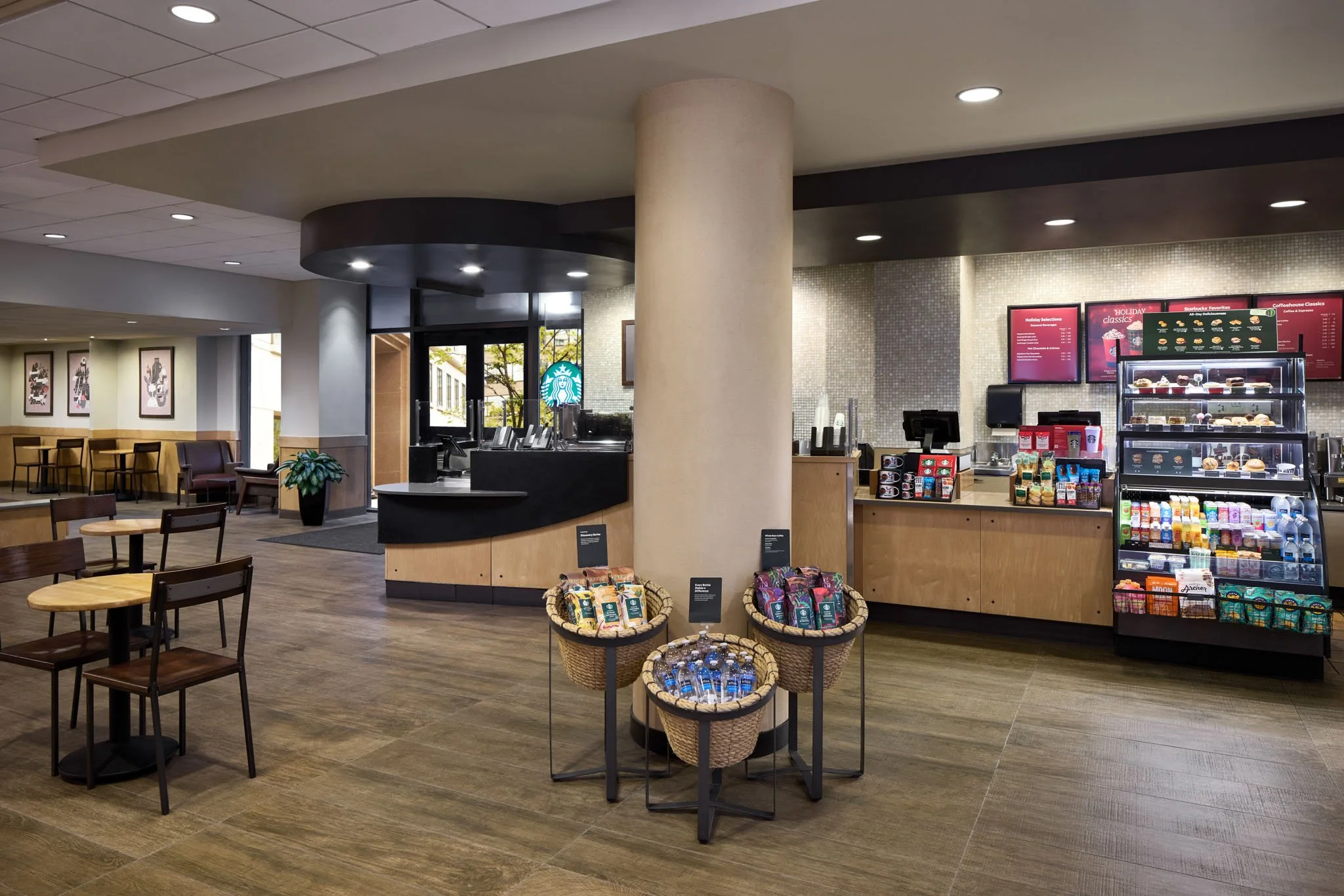 Interior of a Starbucks coffee shop with a counter, display case, tables, and chairs.