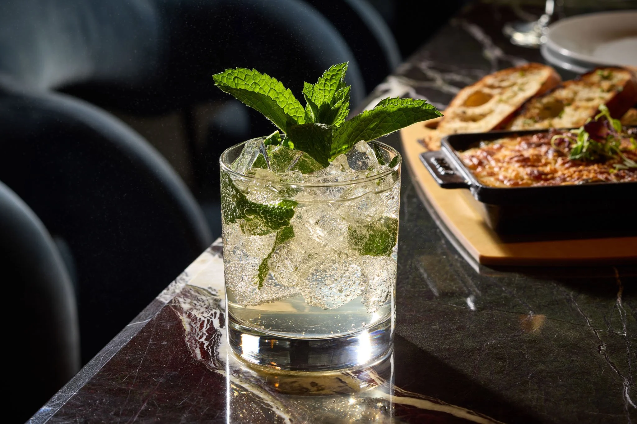A glass of mint mojito with ice and fresh mint leaves, placed on a dark marble table at a restaurant.
