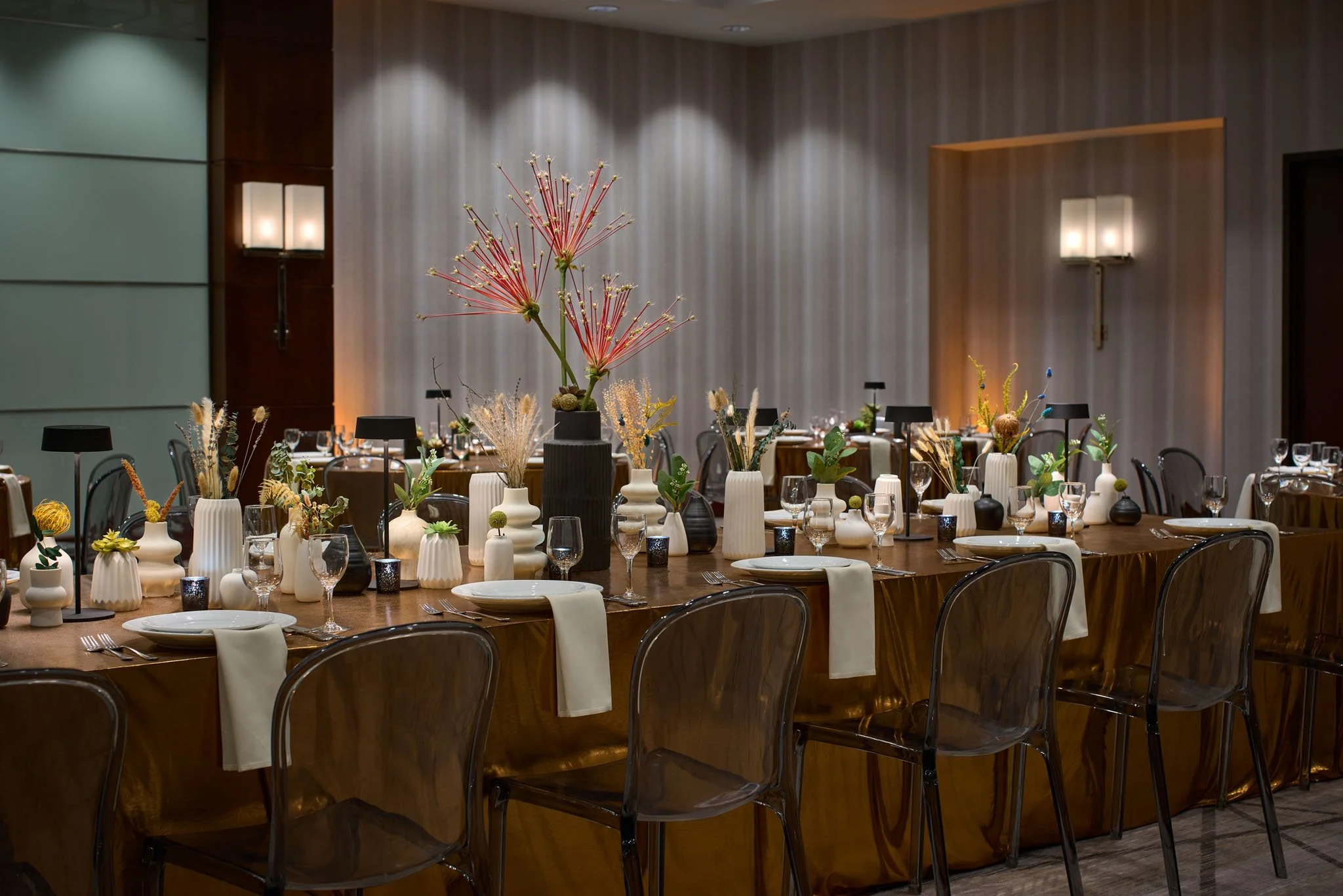 Elegant banquet table setup with vases and floral arrangements in a decorated dining room with warm lighting.