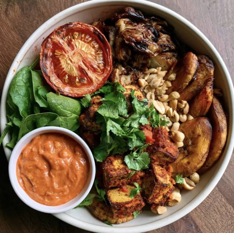 Suya Fiber Bowl with Suya Chickpea-Crusted Baked Tofu, Roasted Sweet Plantains, Braised Smoky Cabbage, Tomatoes, Spinach, Cilantro, Peanuts, Tomato Peanut Sauce