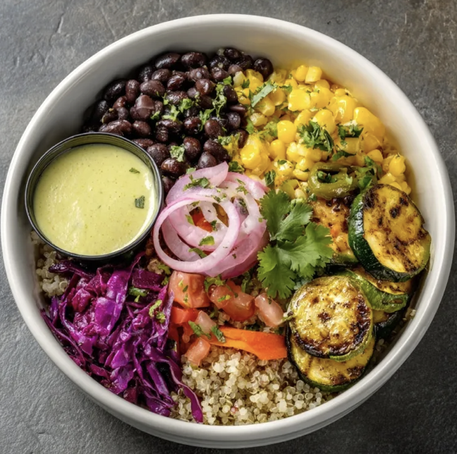 Tropical Nourish Bowl with Black Beans, Corn, Mango, Quinoa, Tomatoes, Carrots, Zucchini, Red Cabbage, Green Peppers, Cilantro, Pickled Onions, Avocado Tahini Sauce