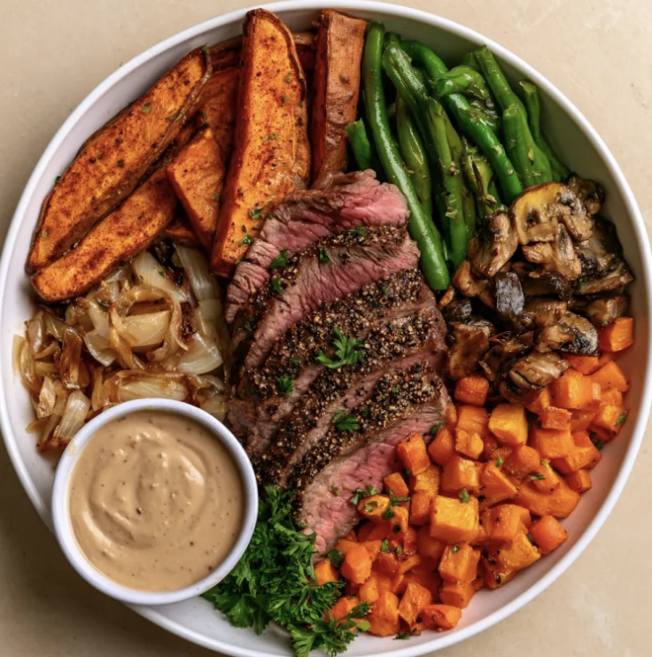 Iron Frites Bowl with Pepper Crusted Steak, Paprika Sweet Potato Wedges, Caramelized Onions, Green Beans, Carrots, Sautéed Mushrooms, Parsley, Au Poivre Sauce