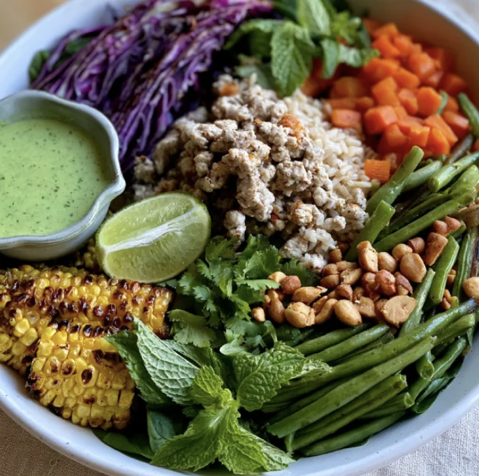 Thai Protein Bowl with Turkey Larb, Brown Rice, Roasted Red Cabbage, Carrots, Green Beans, Sweet Corn, Cilantro, Mint, Peanuts, Lime Wedge, Lime Cilantro Dressing