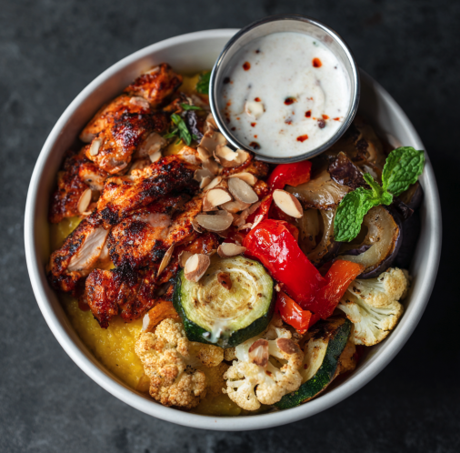Golden Heat Bowl with Smoky Harissa Chicken, Polenta, Steamed Zucchini, Roasted Eggplant, Roasted Cauliflower, Roasted Bell Peppers, Mint, Almonds, Spiced Labneh