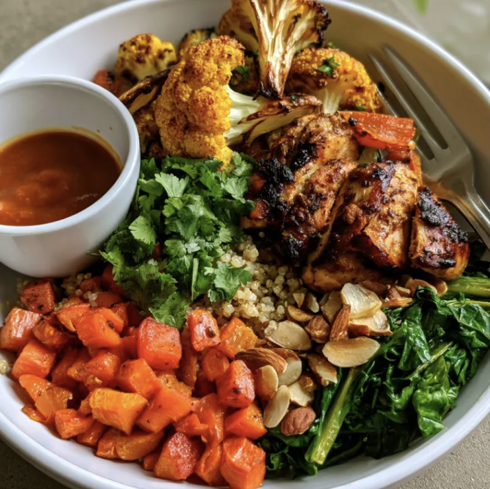 Marrakech Glow Bowl with Moroccan Chicken, Quinoa, Roasted Turmeric Cauliflower, Roasted Carrots, Sautéed Swiss Chard, Cilantro, Almonds, Tajine Sauce