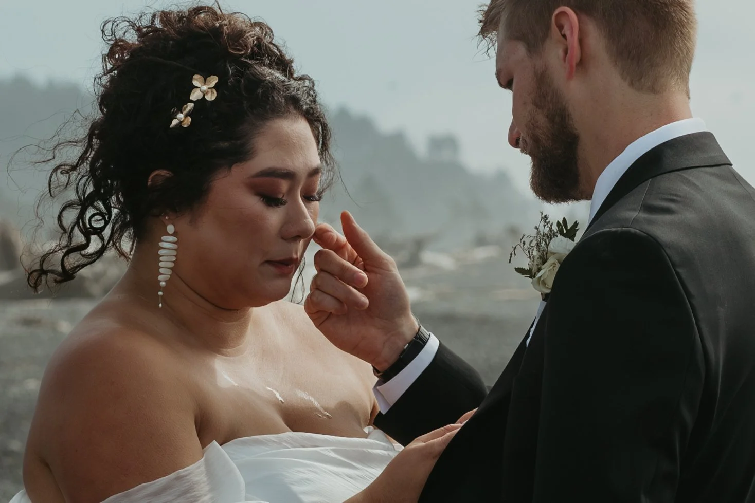A bride and groom in a wedding ceremony, with the groom gently touching the bride's face, outdoors with a blurry background.
