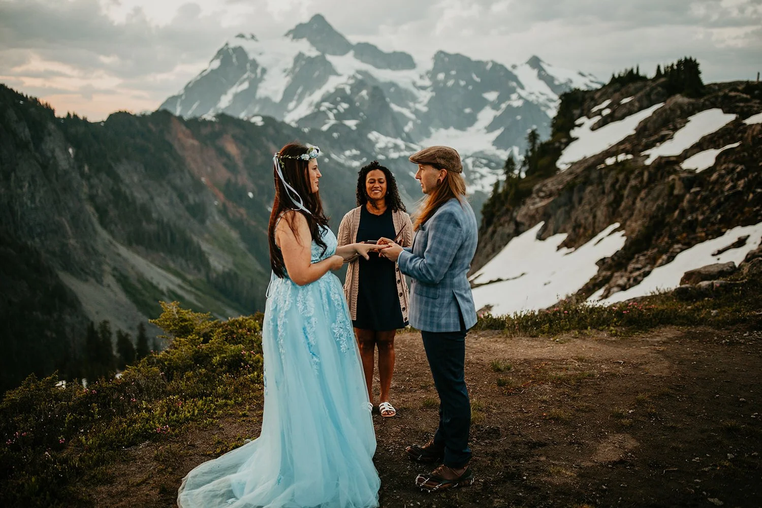 Two people exchanging rings during an intimate mountain elopement ceremony with snowy peaks and an officiant behind them