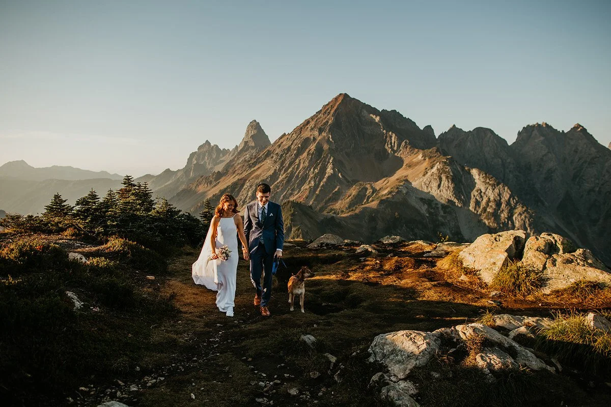 Couple walking their dog along a scenic mountain trail during a dog-friendly Washington elopement at golden hour.