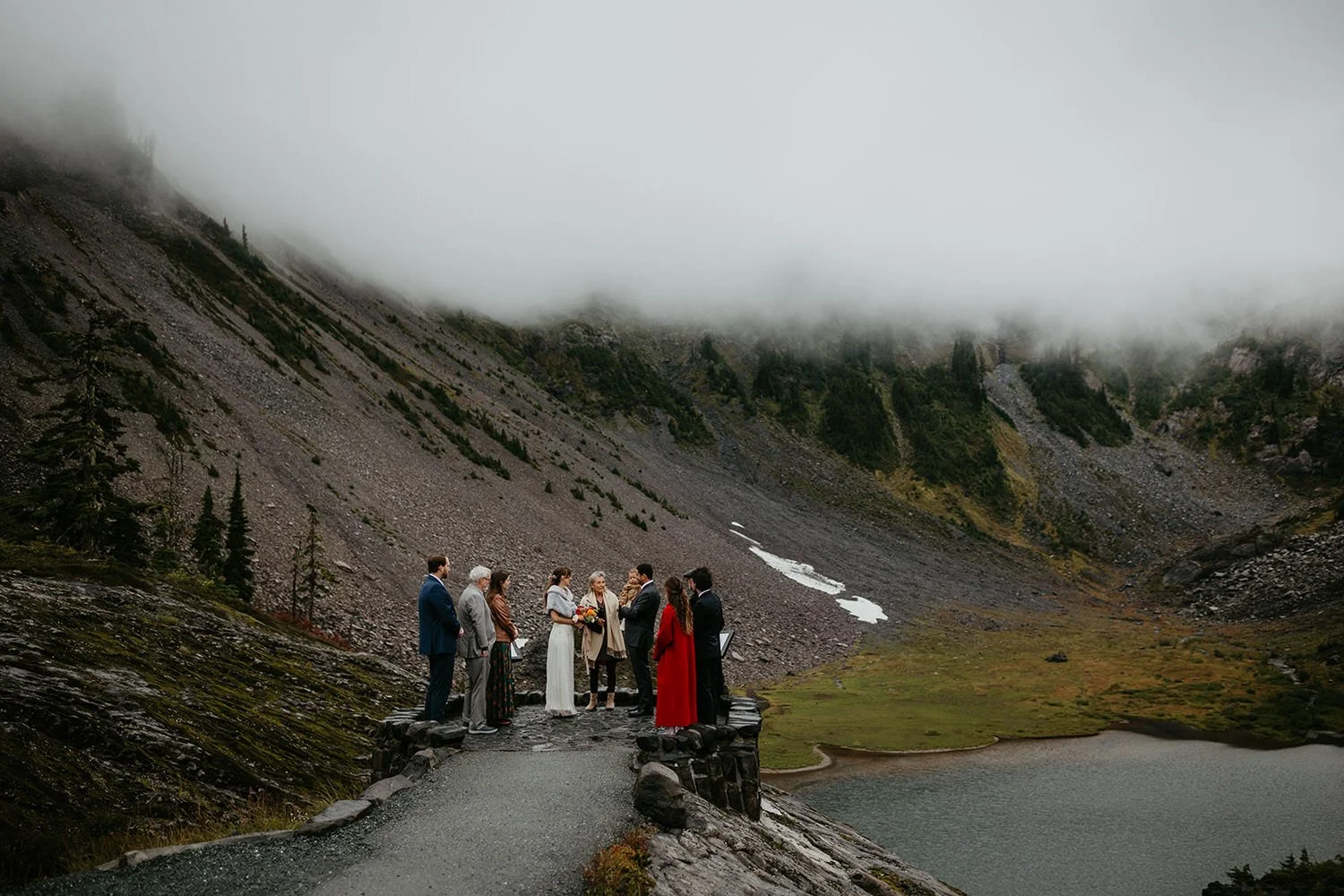 Small elopement ceremony on a stone overlook above an alpine lake with foggy mountain backdrop in Washington