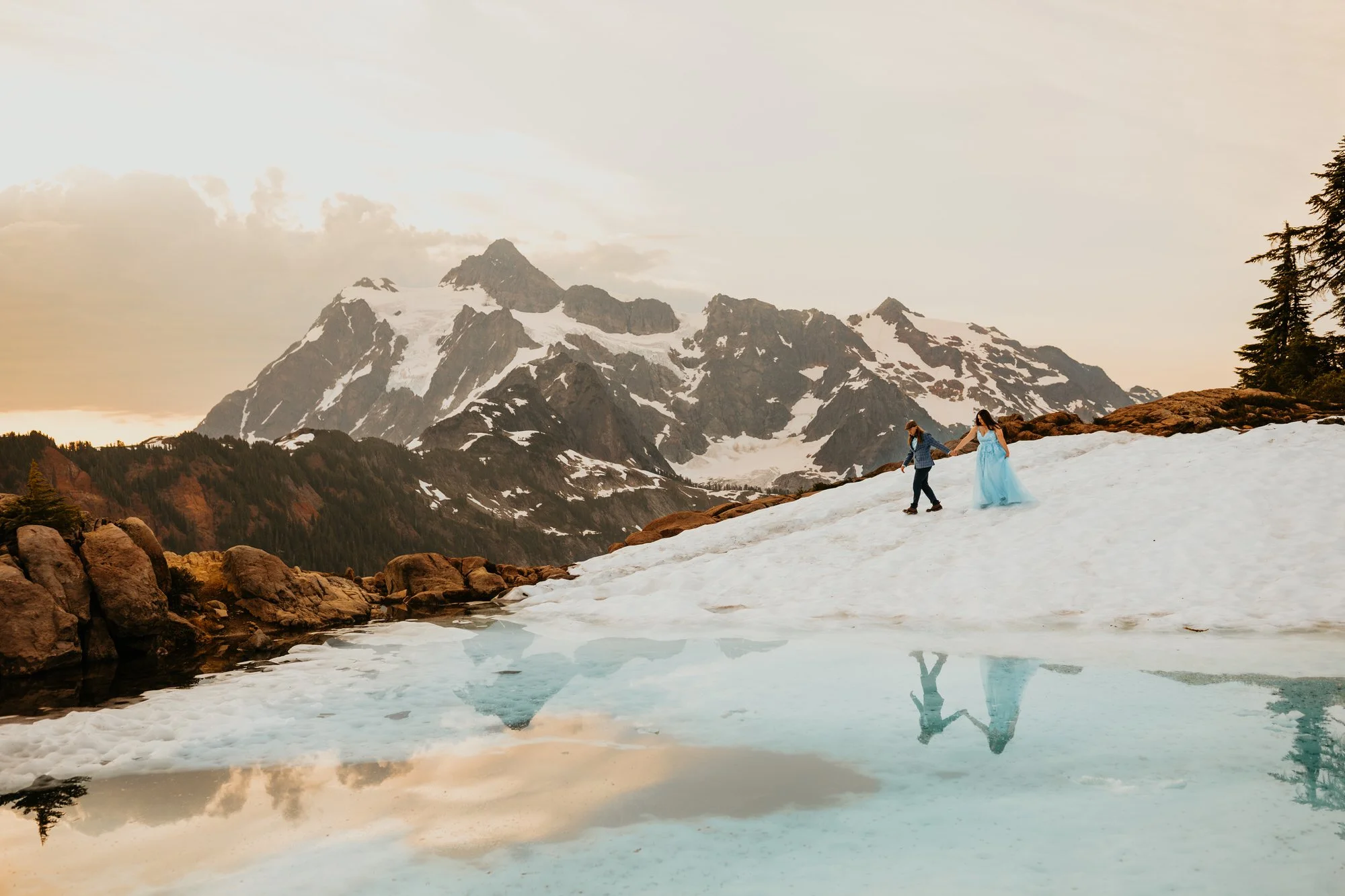 Couple eloping beside a partially frozen alpine lake in the North Cascades with snow-covered mountains in the background