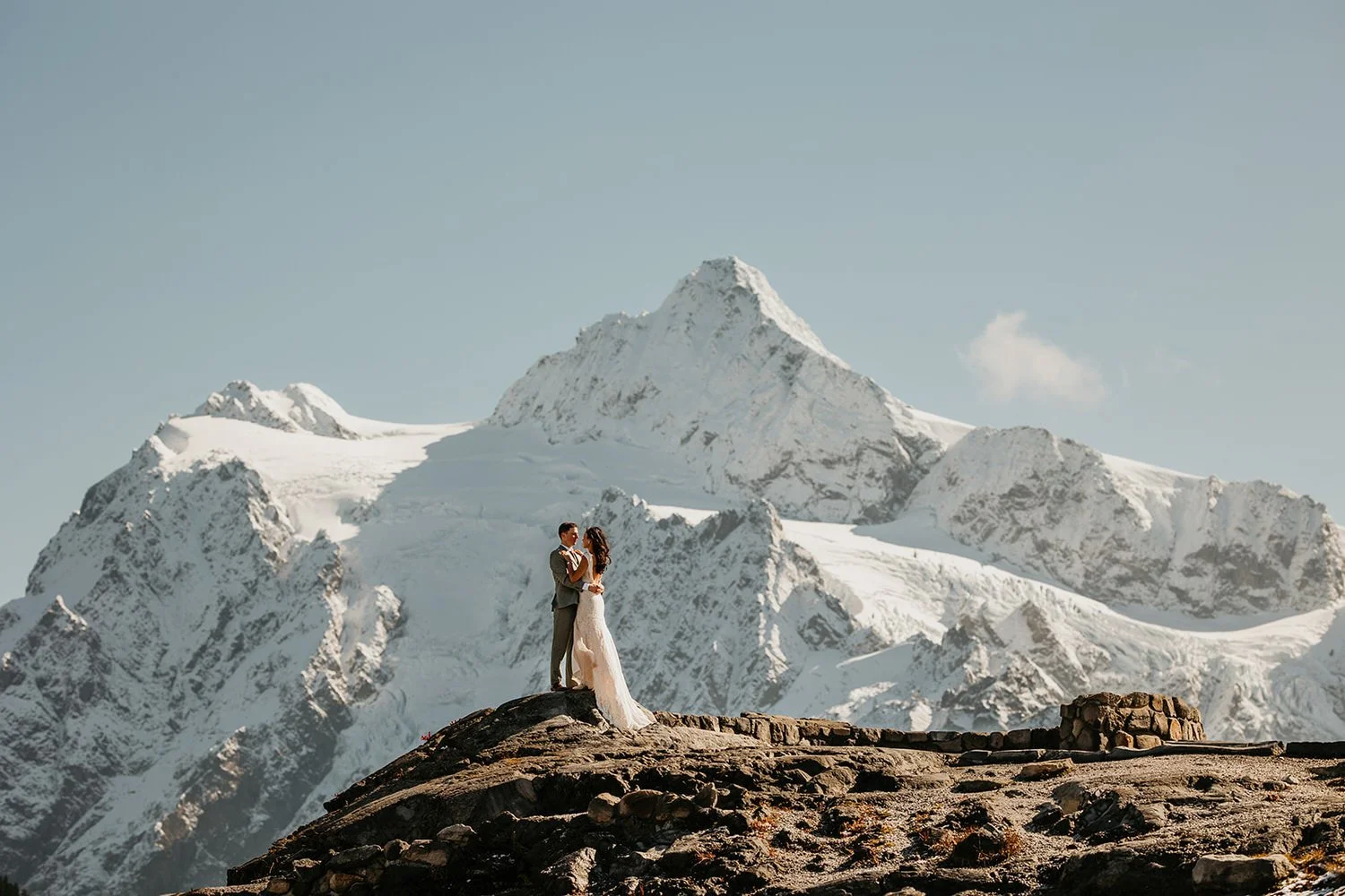Couple embracing atop a stone overlook wall with Mount Shuksan's glaciers filling the skyline