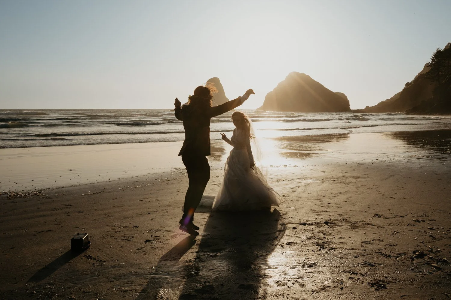Couple dancing barefoot on a Washington beach at sunset with ocean waves and sea stacks in the background.