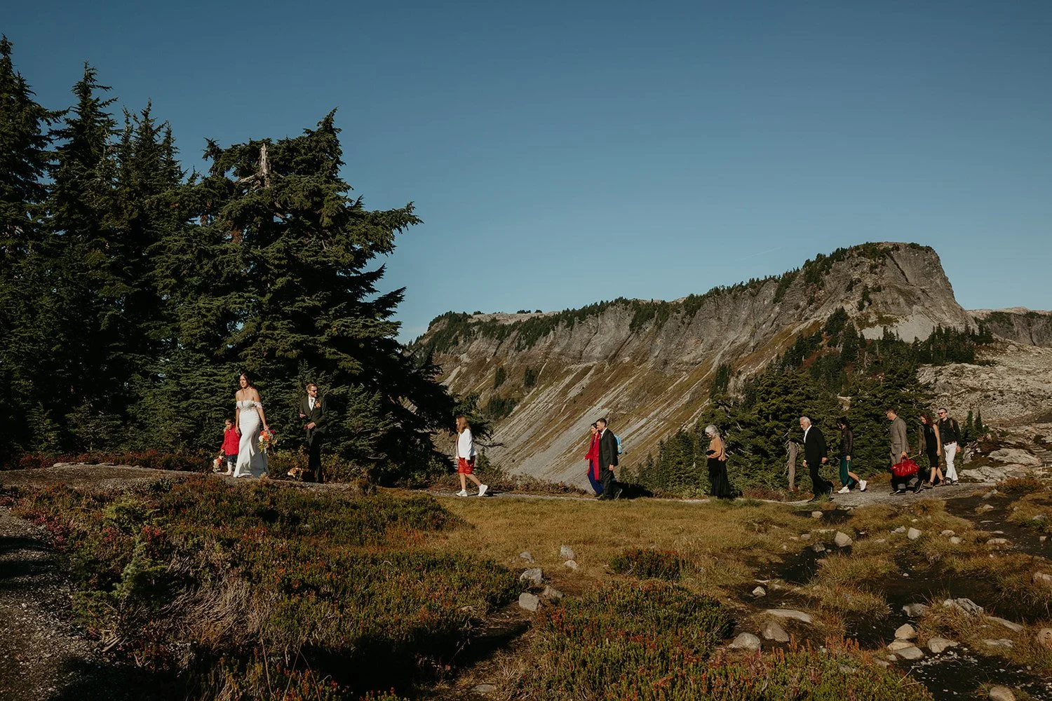 Elopement guests walking along a mountain trail toward a ceremony location in Washington