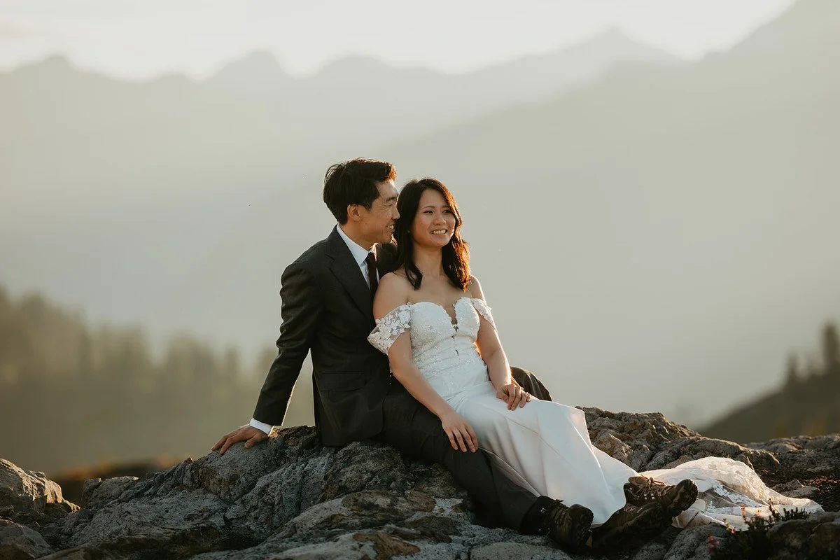 Close portrait of bride and groom sitting on rocks smiling softly in early morning light.jpg