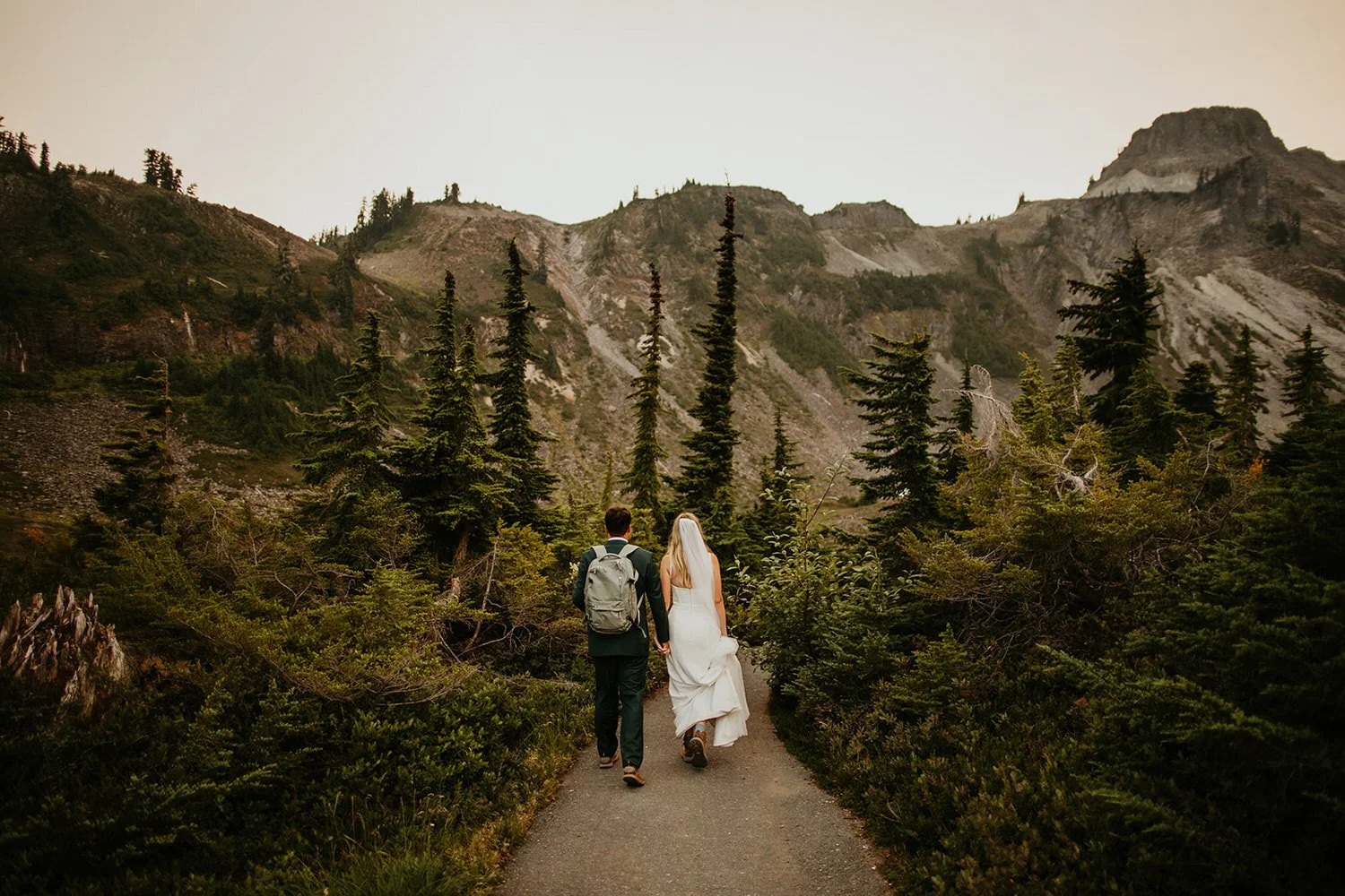 Couple walking hand in hand along a paved mountain path with peaks rising ahead