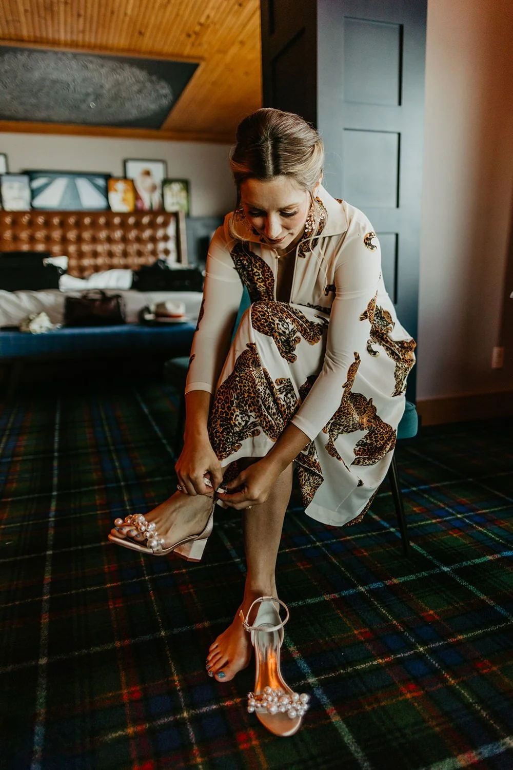 Bride putting on jeweled heels while getting ready on a tartan carpet inside a uniquely decorated cabin Airbnb