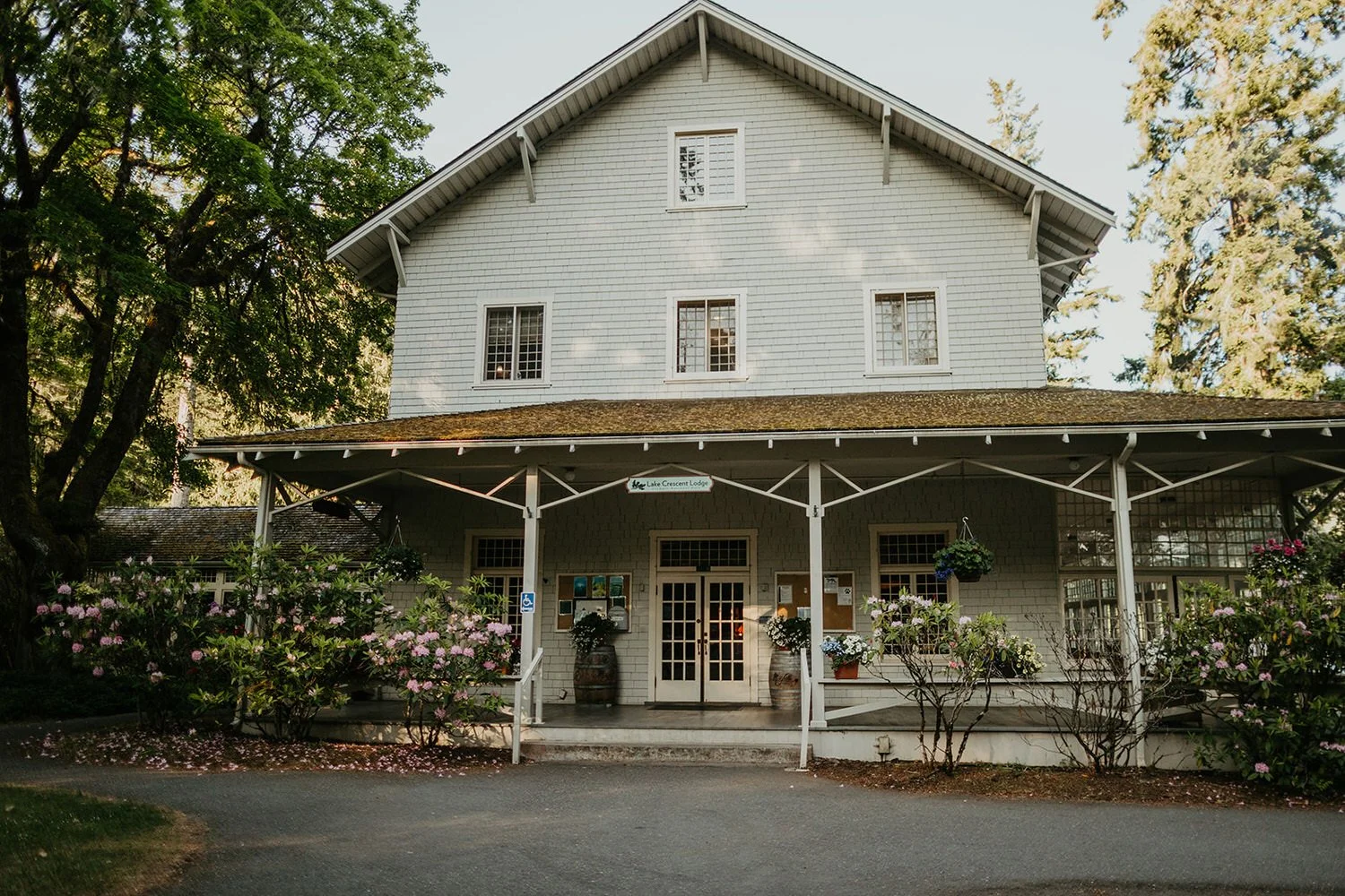 Historic Lake Crescent Lodge with a wide front porch, white siding, and surrounding greenery on a clear summer day.