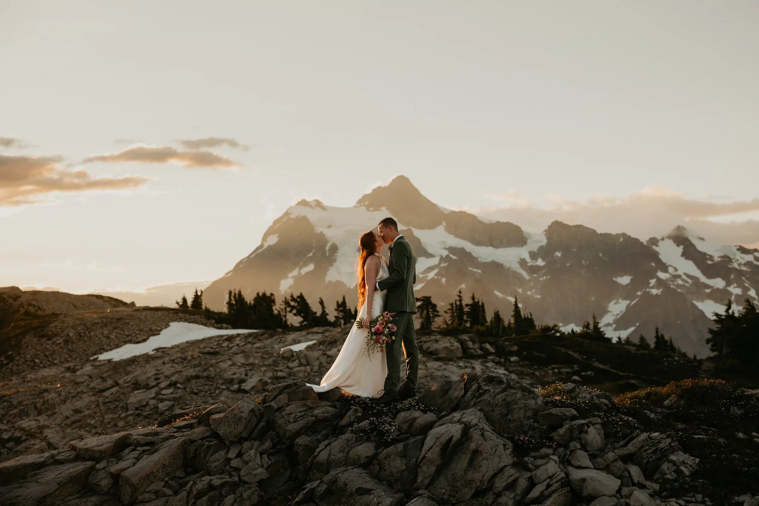 Couple sharing a quiet moment on a rocky alpine overlook at sunset with dramatic mountain peaks behind them.