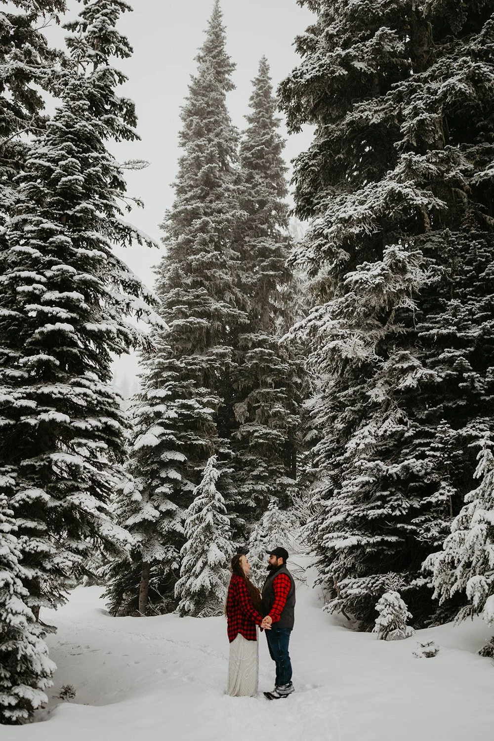 Couple walking hand in hand through a snowy evergreen forest during a winter Washington elopement.