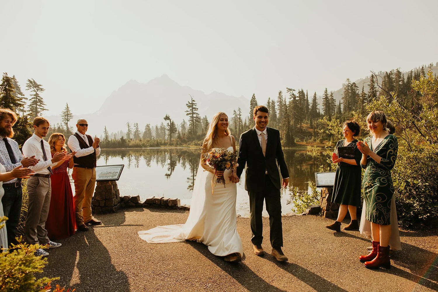 Couple walking together after elopement ceremony beside an alpine lake with guests applauding