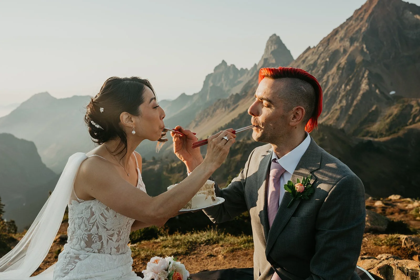 Couple eating cake with chopsticks at a mountain overlook during golden hour on their Washington elopement day.