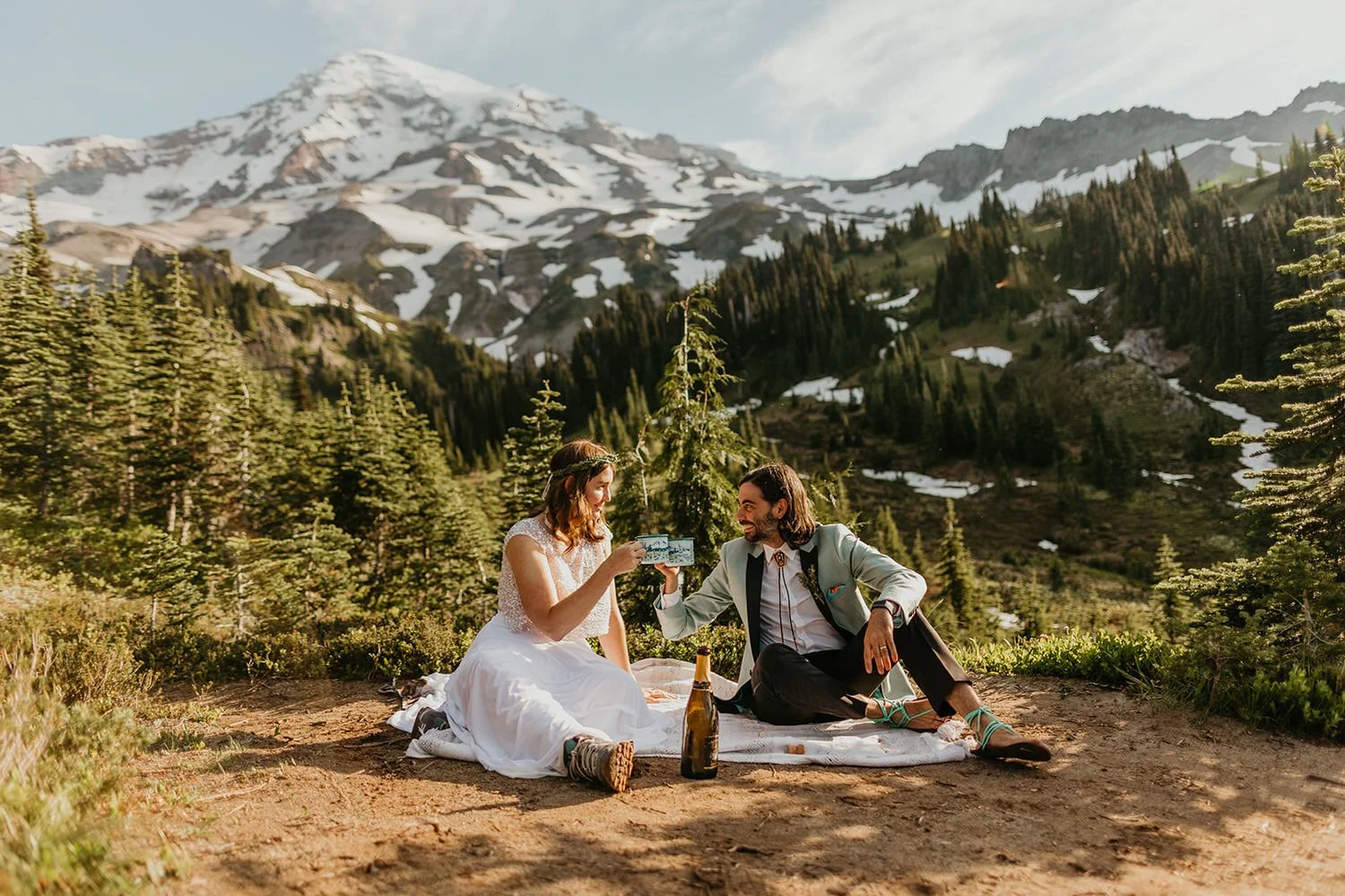 Elopement picnic with a couple seated on a blanket, toasting with champagne in a mountain meadow