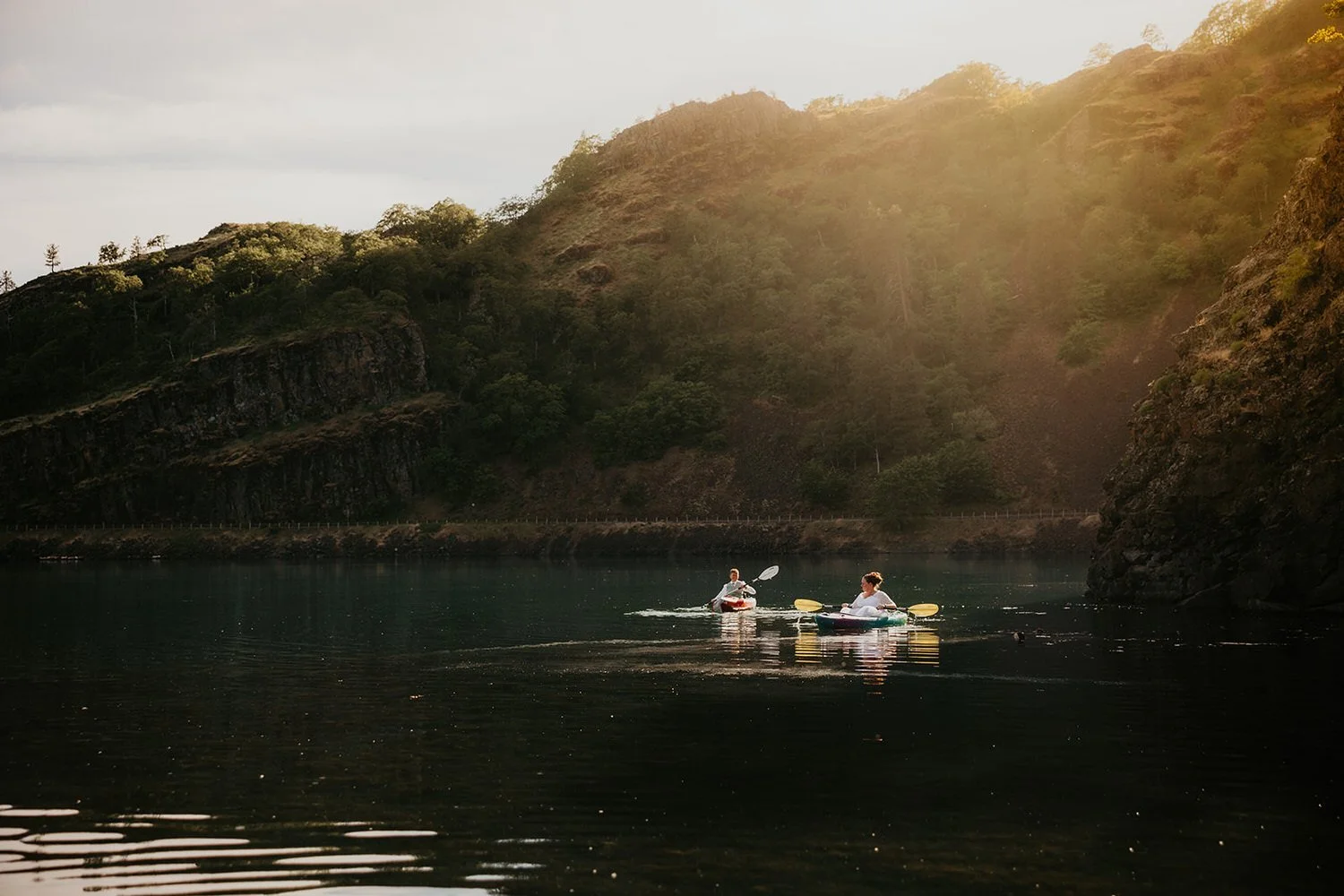 Eloping couple kayaking together on a calm river at sunset with steep canyon walls and golden light reflecting on the water