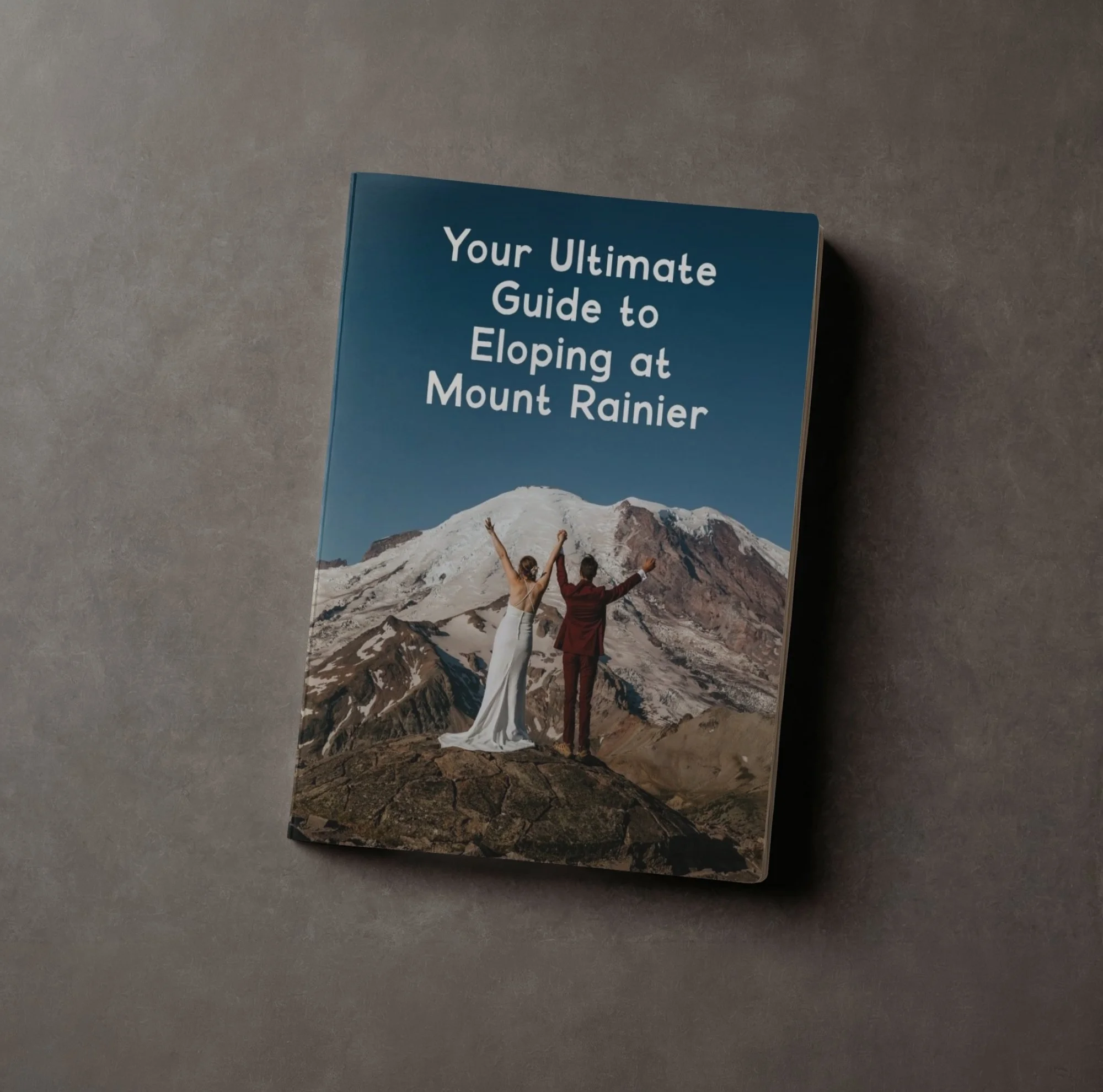 A book titled 'Your Ultimate Guide to Eloping at Mount Rainier' shows a couple celebrating with mountain scenery in the background.