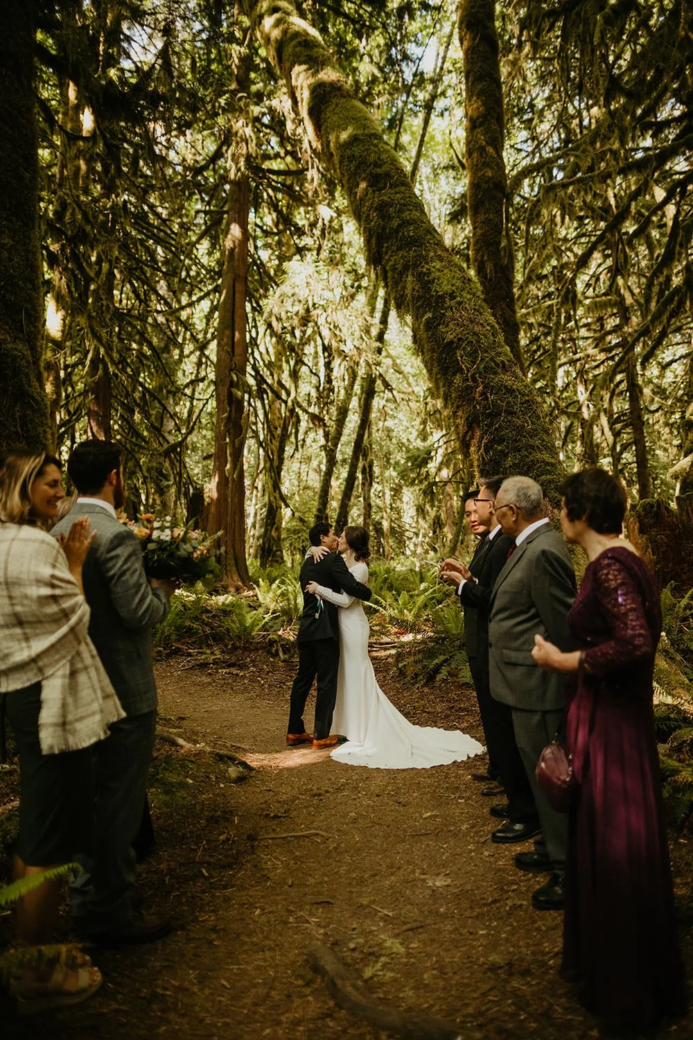 Couple kissing after elopement ceremony in a lush forest surrounded by guests in Washington