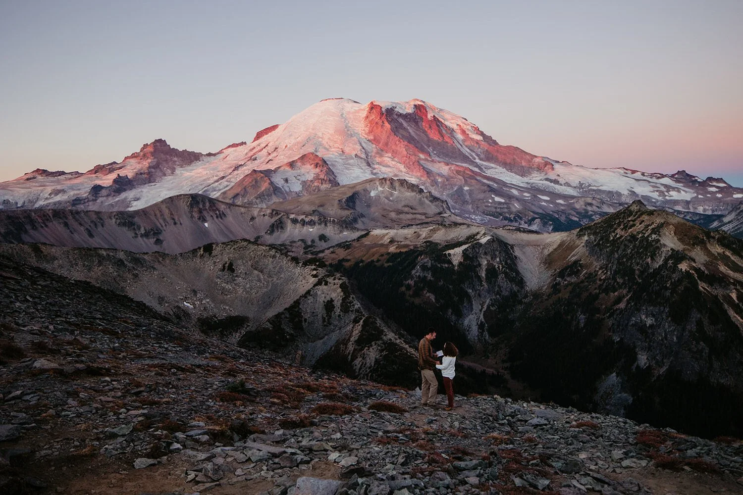 Mount Rainier glowing pink during sunrise above rocky alpine terrain in Washington State.