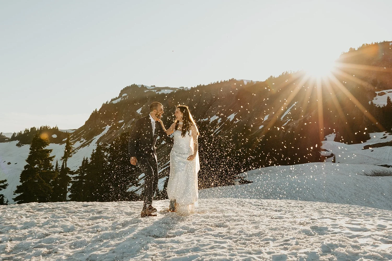 Eloping couple kicking up fresh snow at sunset in North Cascades National Park, celebrating their wedding day in a quiet alpine setting