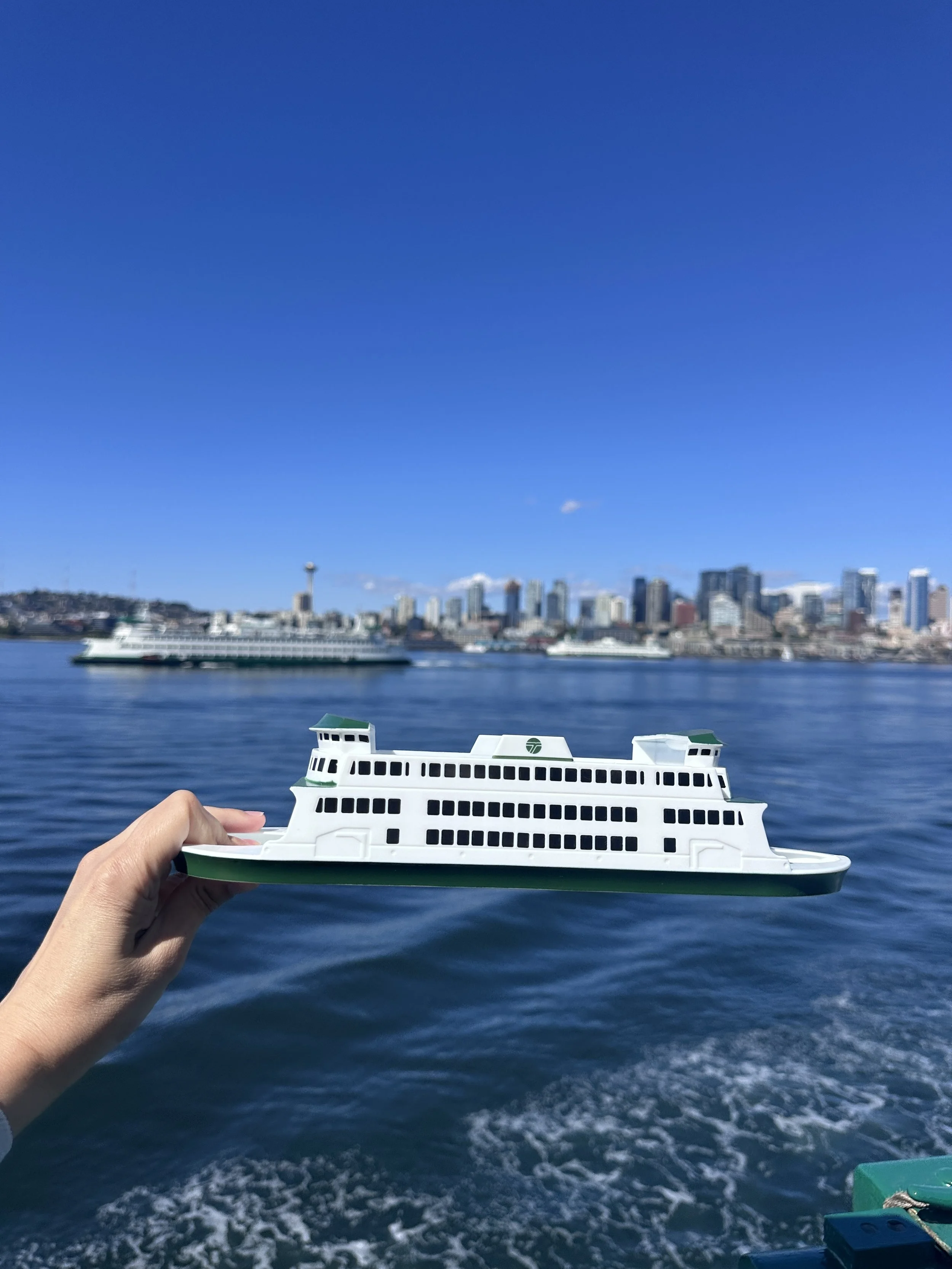 Washington state ferry boat souvenir held up in front of the Space Needle and Seattle's waterfront
