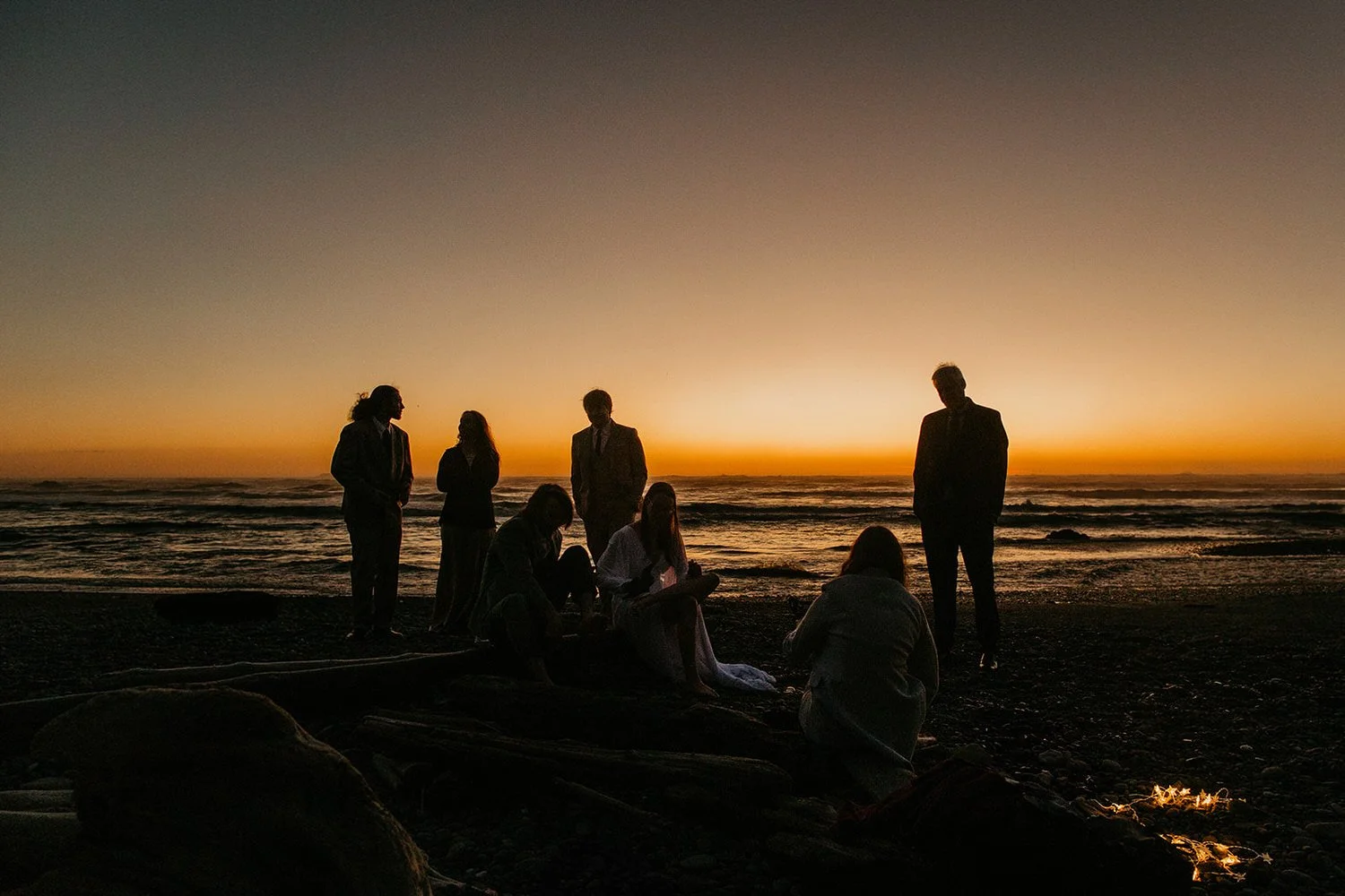 Elopement group gathered on a beach at sunset with silhouettes against the ocean