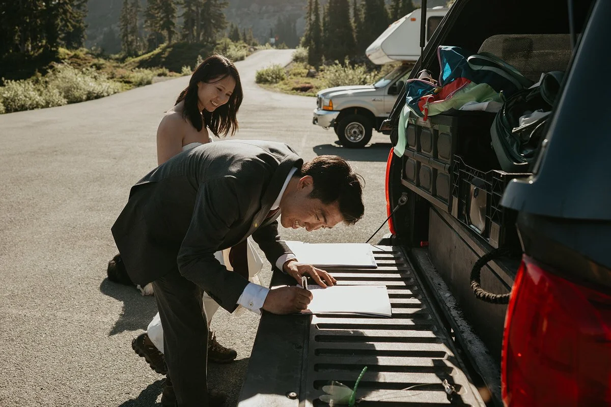 Groom signs marriage license paperwork on the tailgate of a truck in a Washington mountain parking lot before their elopement ceremony.