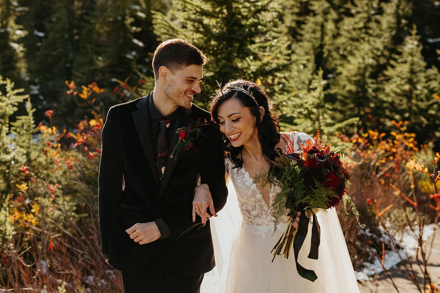 Couple walking arm in arm through an evergreen forest during an elopement day, laughing together with fall colors and soft natural light