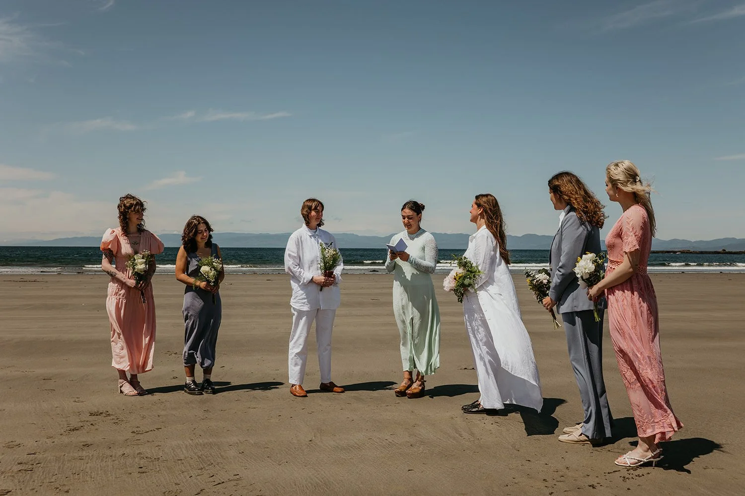 Small queer wedding ceremony on a beach with guests standing in a circle along the Washington coast