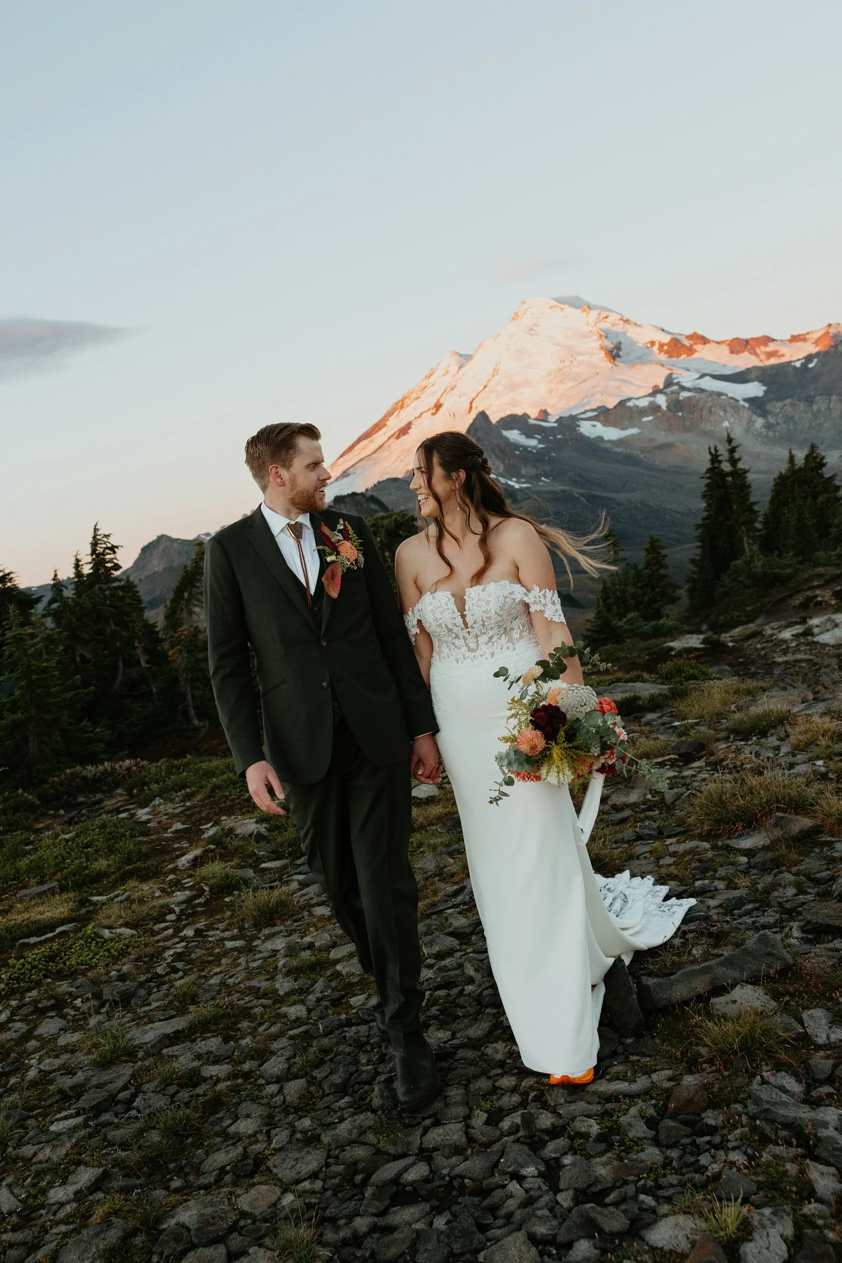 Couple walking hand in hand during sunrise summit portraits in the mountains