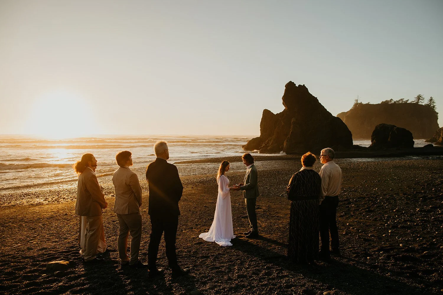 Small beach elopement ceremony at sunset with couple exchanging vows in front of family on the Washington coast