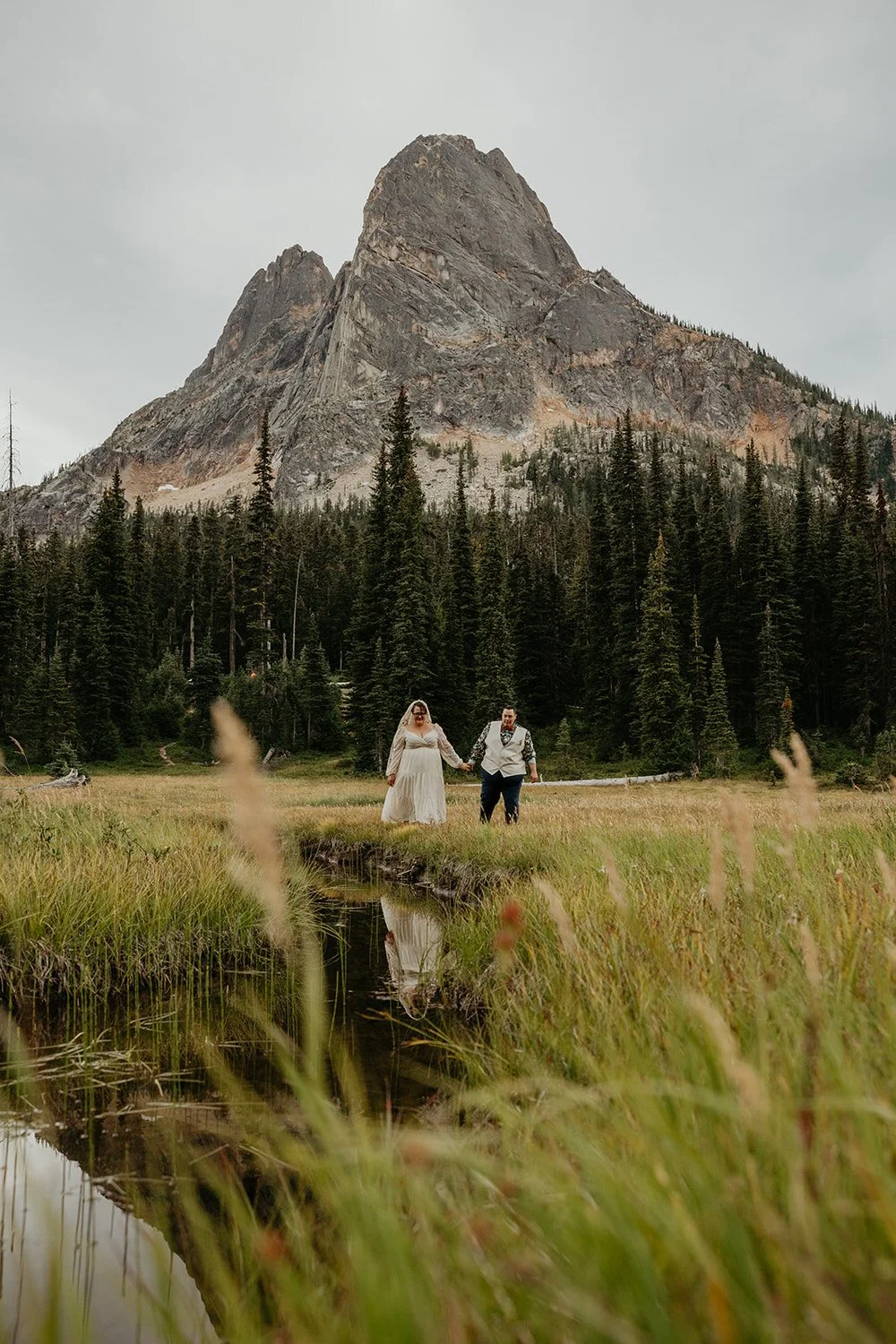 Queer couple stands under Liberty Bell in the North Cascades along a snaking river and tall grass