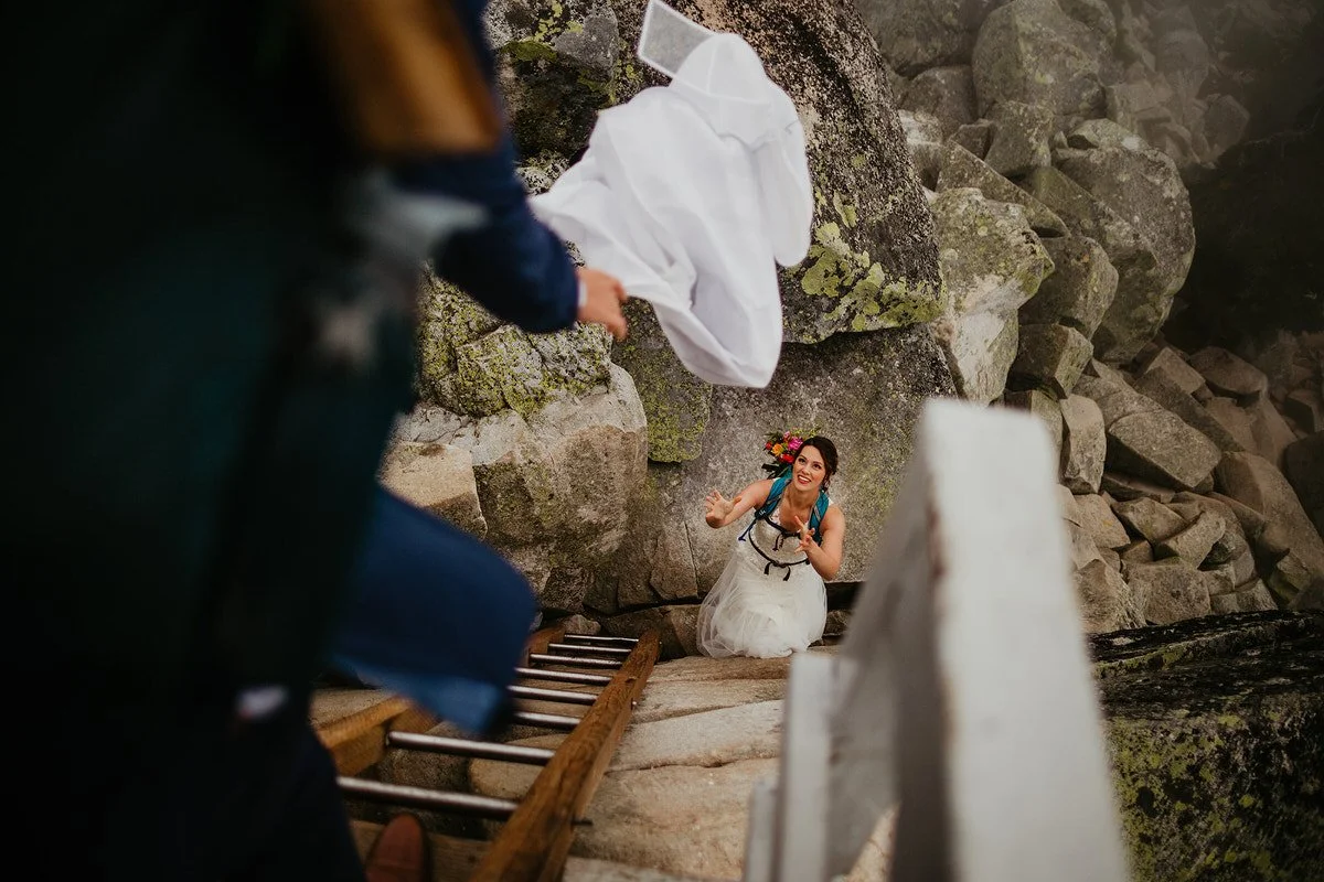 Bride climbing down a wooden ladder at a fire lookout during an adventurous Washington hiking elopement.
