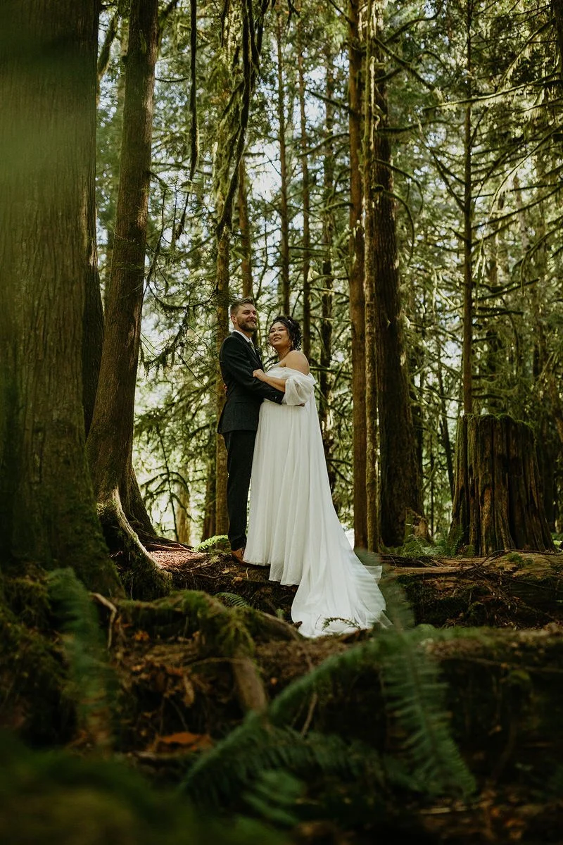 Bride and groom standing in a quiet forest clearing during a Washington elopement, surrounded by tall evergreen trees and soft natural light.