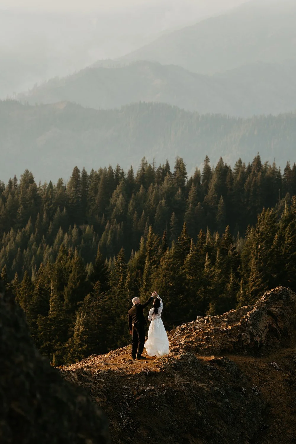 Couple exchanging vows on a dramatic rocky mountain overlook surrounded by dense evergreen forest and misty mountain ridgelines during a Washington elopement