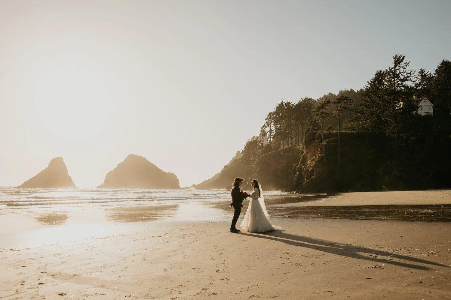 Beach elopement portrait with a couple standing together as the sun sets over the Oregon coast.