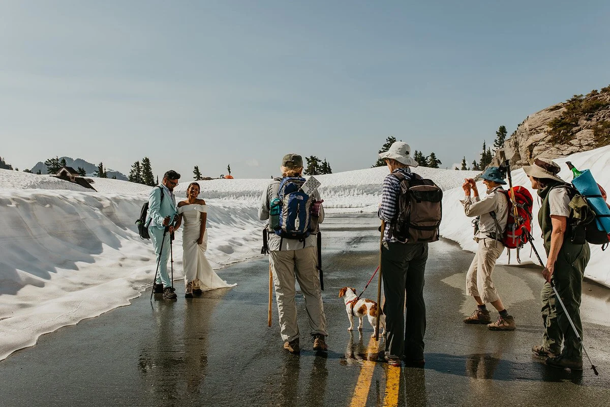 Eloping couple standing on a snowy mountain road while hikers pause nearby during a Washington national park ceremony