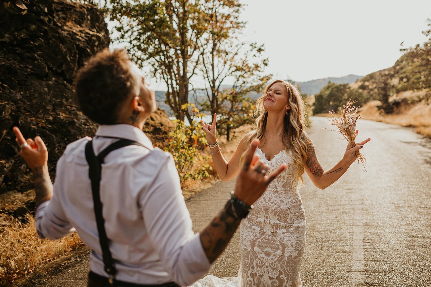 Couple laughing and throwing up rock hand signs while celebrating on a quiet road after their elopement.