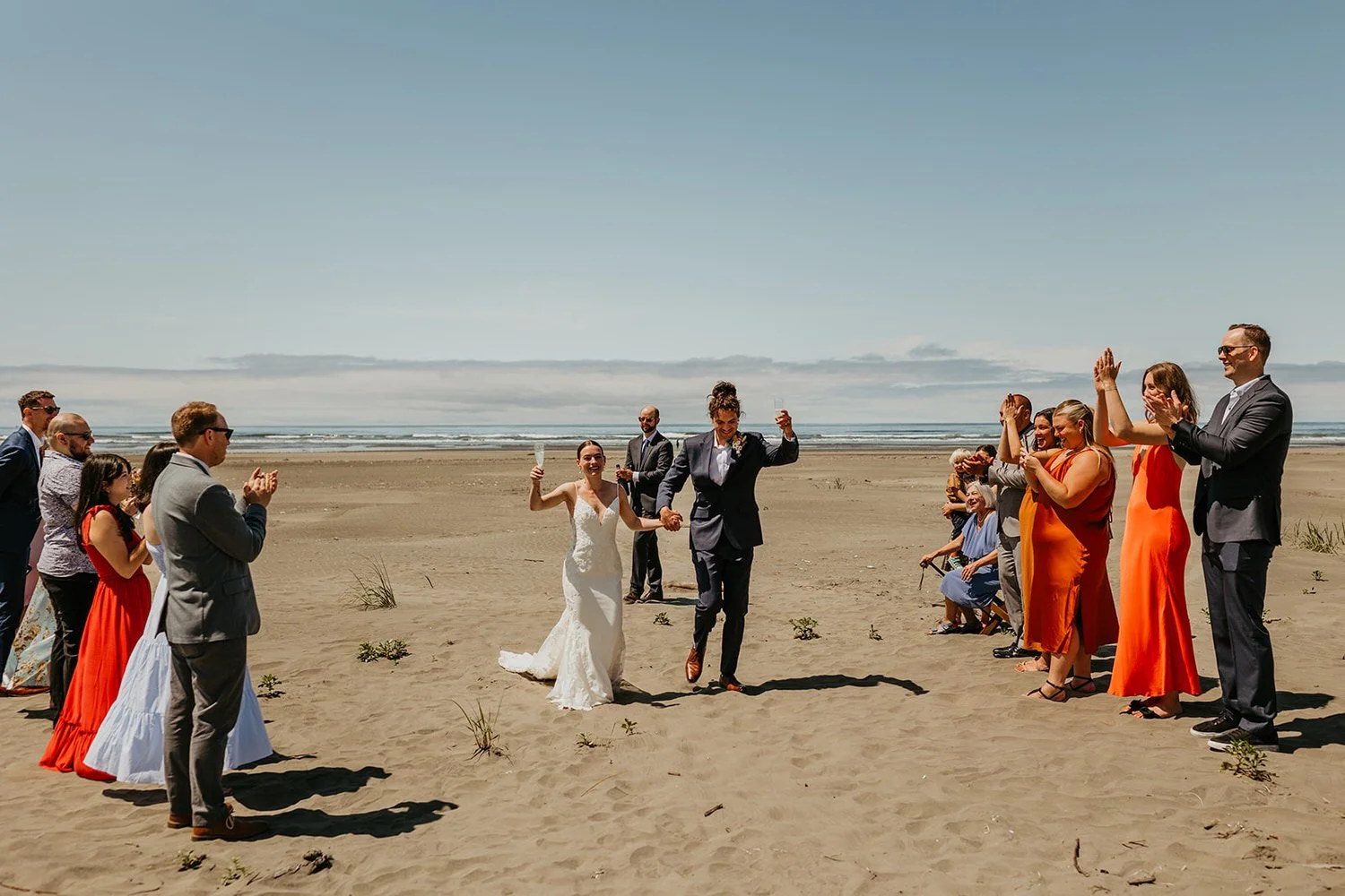 Couple walking down a sandy beach aisle after their elopement ceremony with guests cheering