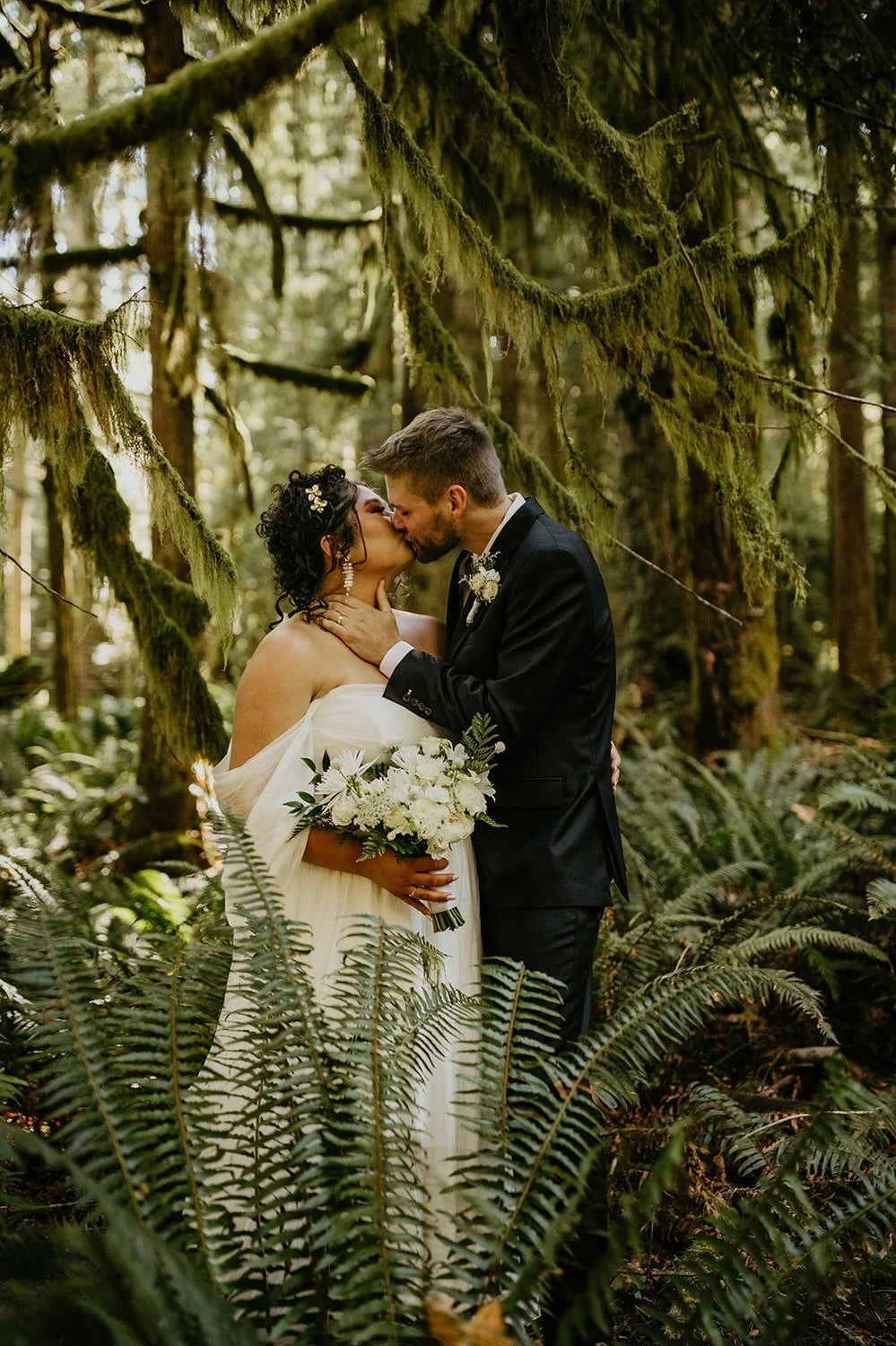 Couple embracing in a mossy forest in Washington, surrounded by ferns and soft filtered light